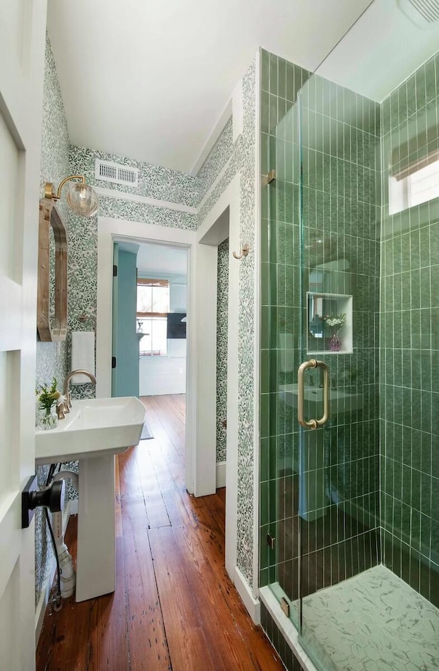 full bath featuring wallpapered walls, visible vents, hardwood / wood-style flooring, a shower stall, and a sink