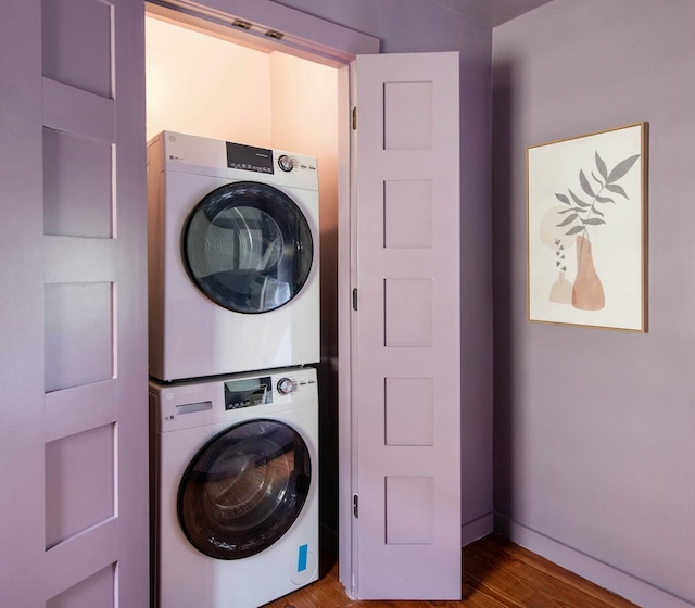 laundry room with wood finished floors, stacked washer and clothes dryer, baseboards, and laundry area