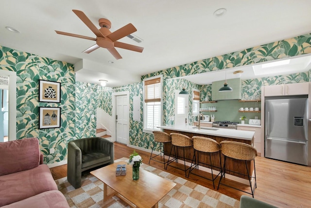 living area with wallpapered walls, stairs, baseboards, and light wood-style floors