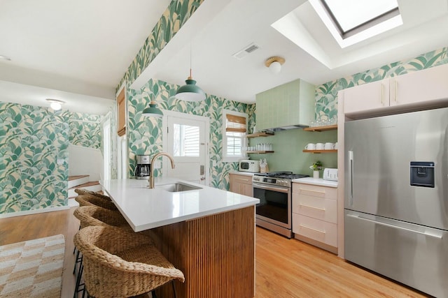 kitchen featuring stainless steel appliances, a sink, light countertops, open shelves, and wallpapered walls