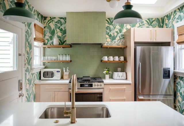 kitchen with wallpapered walls, appliances with stainless steel finishes, light countertops, and a sink