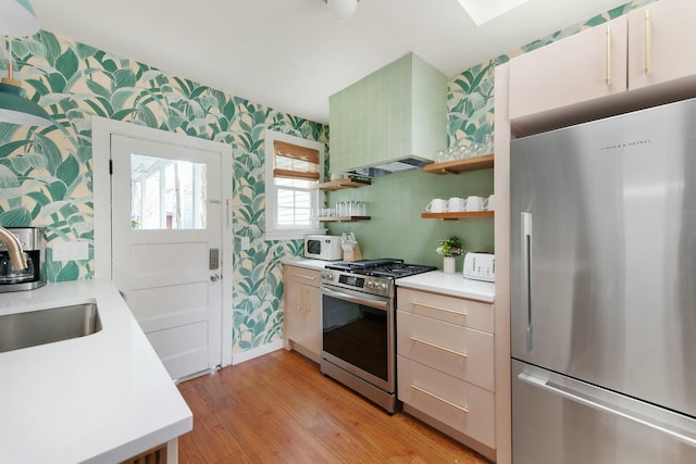 kitchen with open shelves, light countertops, appliances with stainless steel finishes, wall chimney exhaust hood, and wallpapered walls