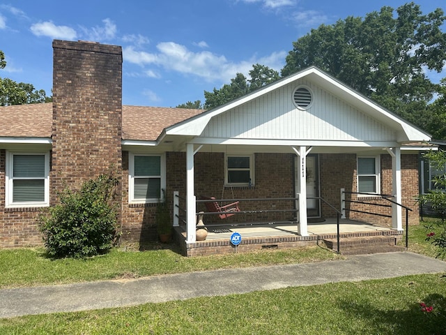 view of front of home featuring a shingled roof, covered porch, a chimney, and brick siding