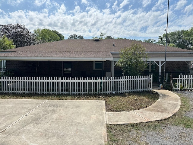 back of house featuring brick siding, a shingled roof, and a fenced front yard