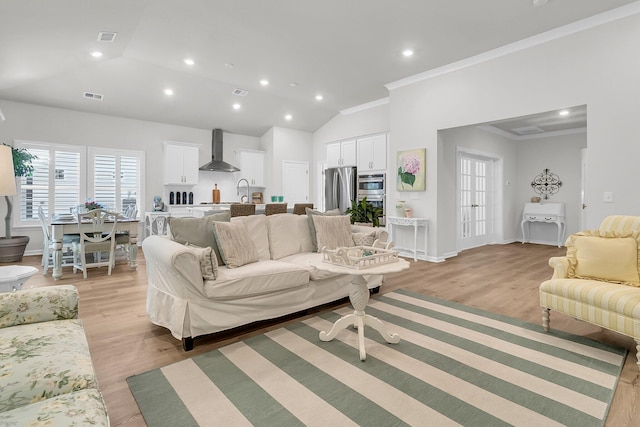 living room featuring lofted ceiling, light wood-type flooring, and crown molding