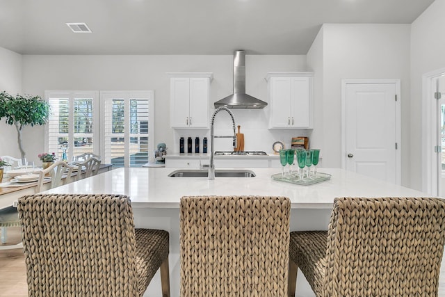 kitchen featuring white cabinets, a breakfast bar area, wall chimney exhaust hood, and a large island