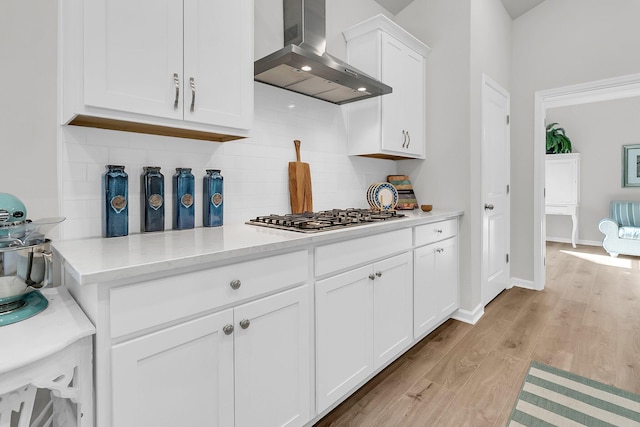 kitchen with backsplash, light stone counters, wall chimney range hood, white cabinetry, and stainless steel gas stovetop