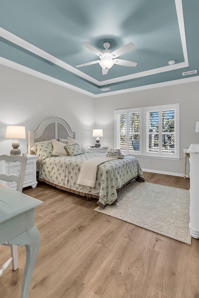 bedroom featuring ceiling fan, light hardwood / wood-style floors, and a tray ceiling