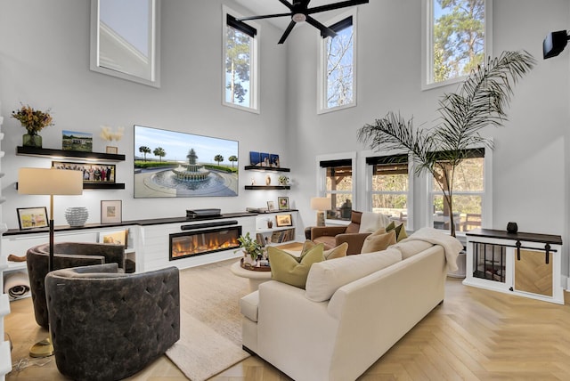 living area featuring a high ceiling, a glass covered fireplace, and a ceiling fan