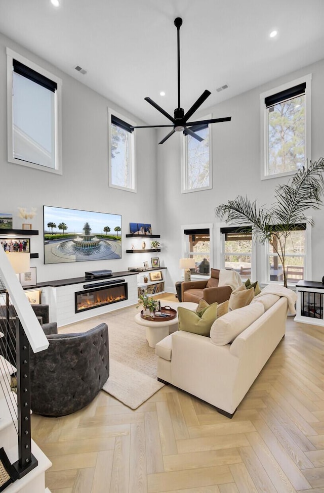 living area featuring a towering ceiling, recessed lighting, visible vents, and a glass covered fireplace