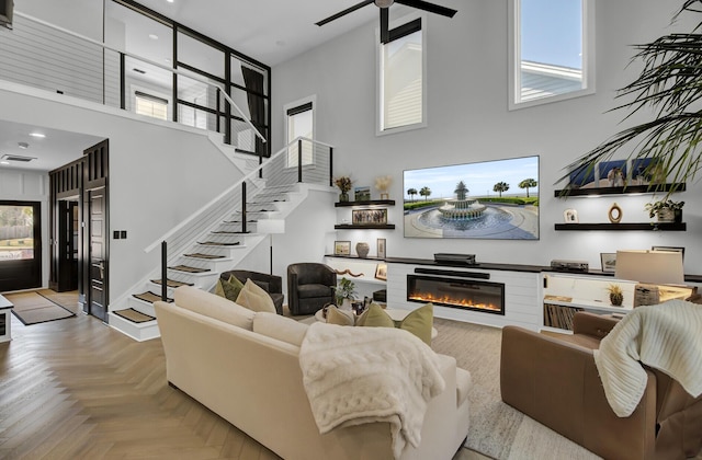 living area with stairway, a high ceiling, a ceiling fan, a glass covered fireplace, and baseboards