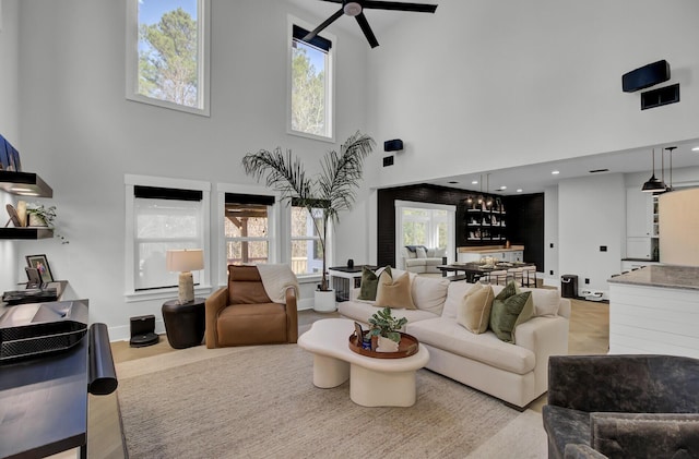 living area featuring baseboards, ceiling fan, a towering ceiling, and light wood-style floors