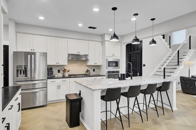 kitchen with under cabinet range hood, stainless steel appliances, a sink, white cabinets, and tasteful backsplash