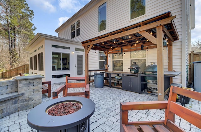 view of patio / terrace with a sunroom, an outdoor fire pit, and fence