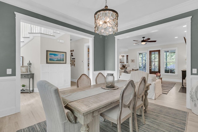dining space featuring light wood-style flooring, ornamental molding, a chandelier, and a ceiling fan