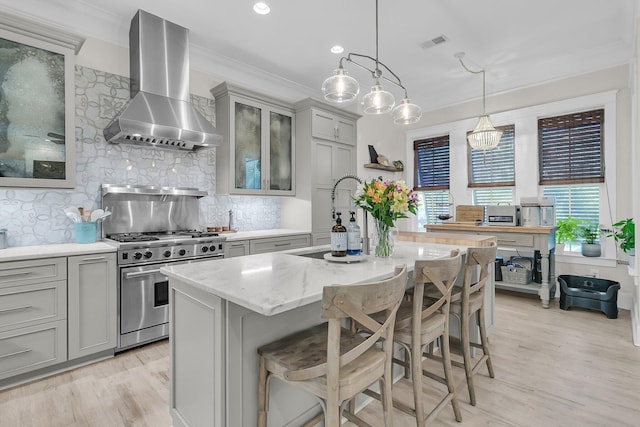 kitchen with wall chimney range hood, stainless steel stove, gray cabinetry, crown molding, and light wood-style flooring