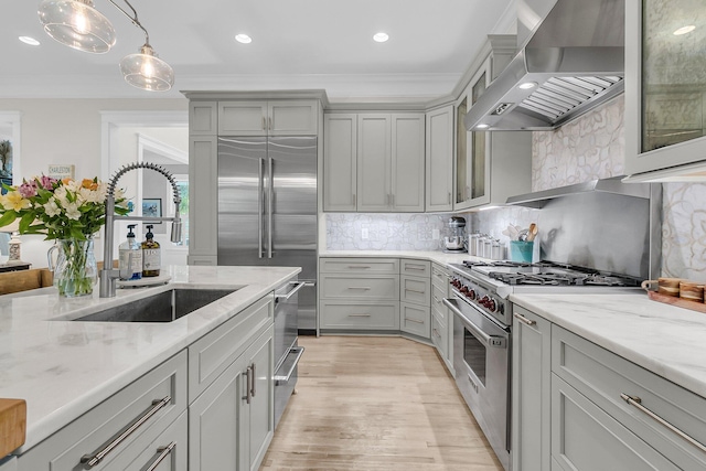 kitchen featuring high quality appliances, wall chimney exhaust hood, gray cabinets, a sink, and decorative backsplash