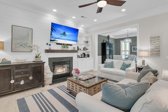 living room featuring crown molding, light wood finished floors, a ceiling fan, a glass covered fireplace, and a chandelier