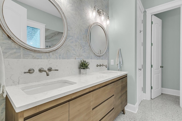 bathroom with baseboards, wallpapered walls, speckle patterned floor, and double vanity