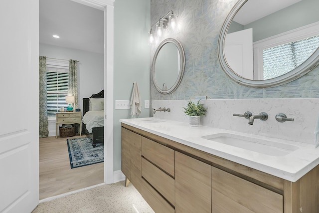 ensuite bathroom featuring wallpapered walls, double vanity, baseboards, and recessed lighting