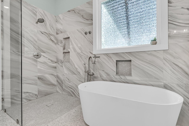 bathroom with a marble finish shower, a freestanding bath, and tile walls