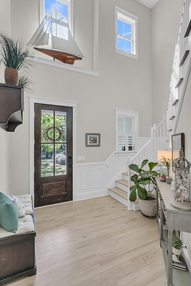 entryway with stairs, a towering ceiling, a wainscoted wall, light wood-style floors, and a decorative wall