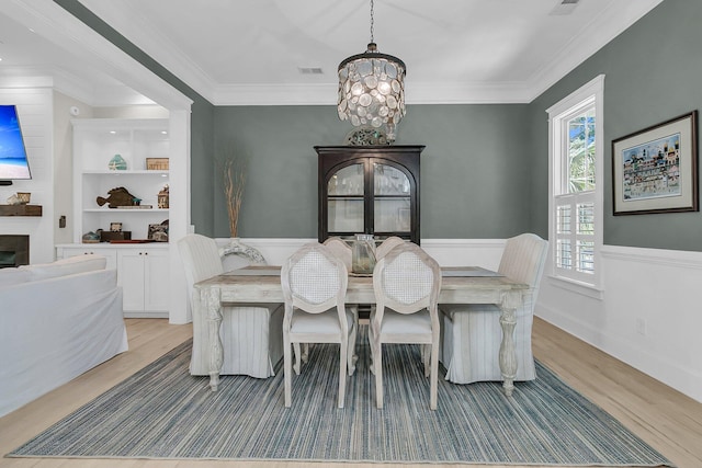 dining room with light wood-type flooring, a chandelier, plenty of natural light, crown molding, and a fireplace