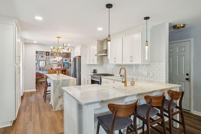 kitchen featuring wall chimney range hood, appliances with stainless steel finishes, hanging light fixtures, a breakfast bar area, and kitchen peninsula