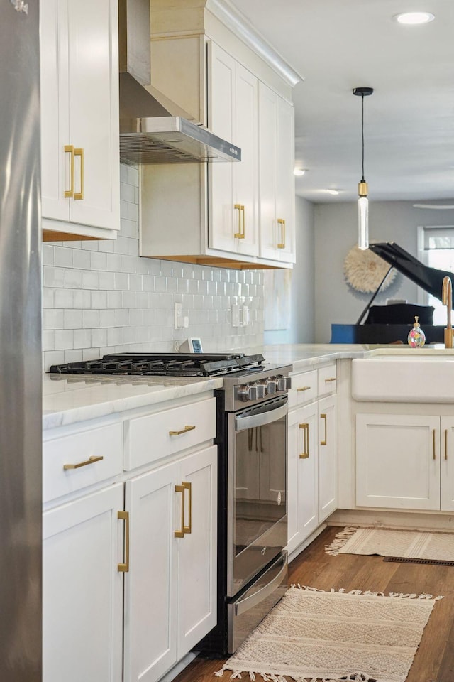 kitchen with stainless steel appliances, dark wood-type flooring, pendant lighting, wall chimney exhaust hood, and white cabinetry