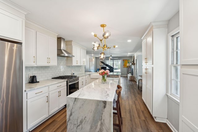 kitchen with stainless steel appliances, wall chimney range hood, decorative light fixtures, a kitchen bar, and dark hardwood / wood-style flooring