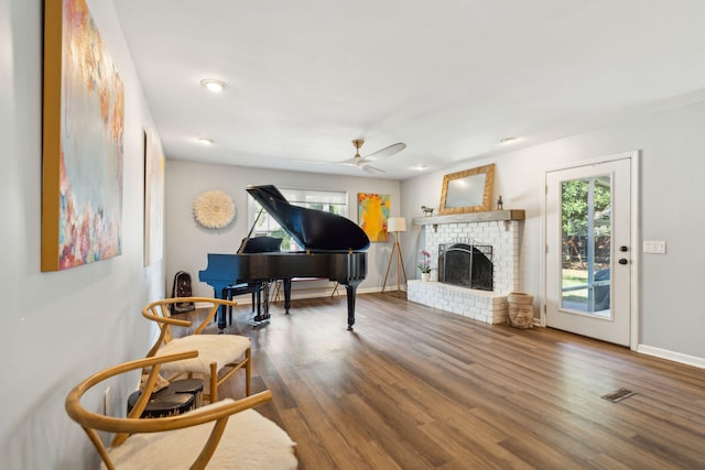 sitting room featuring hardwood / wood-style floors, ceiling fan, and a brick fireplace