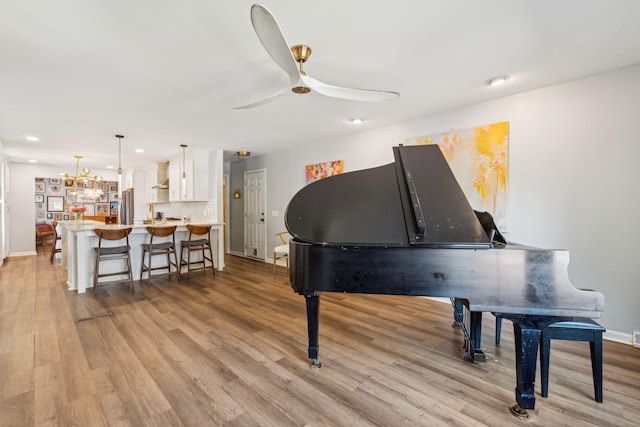 miscellaneous room featuring light wood-type flooring and ceiling fan with notable chandelier