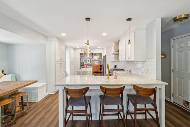 kitchen featuring tasteful backsplash, white cabinetry, decorative light fixtures, dark hardwood / wood-style flooring, and kitchen peninsula