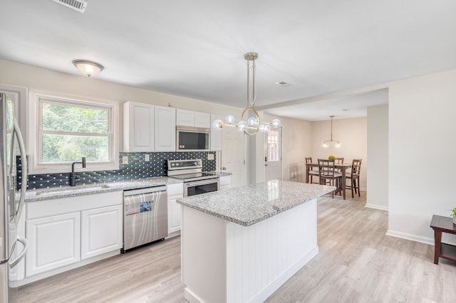 kitchen featuring decorative light fixtures, appliances with stainless steel finishes, white cabinets, and light stone countertops