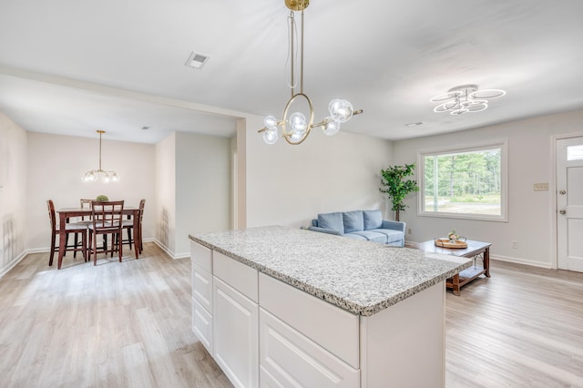 kitchen featuring light wood-type flooring, pendant lighting, white cabinetry, light stone counters, and an inviting chandelier