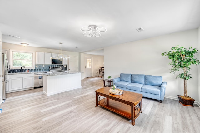 living room with an inviting chandelier, sink, and light hardwood / wood-style flooring