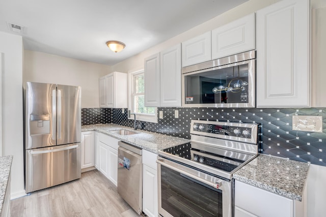 kitchen with stainless steel appliances, sink, light stone countertops, white cabinets, and light hardwood / wood-style floors