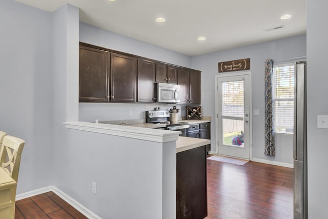 kitchen featuring kitchen peninsula, dark brown cabinets, dark hardwood / wood-style flooring, and stainless steel appliances