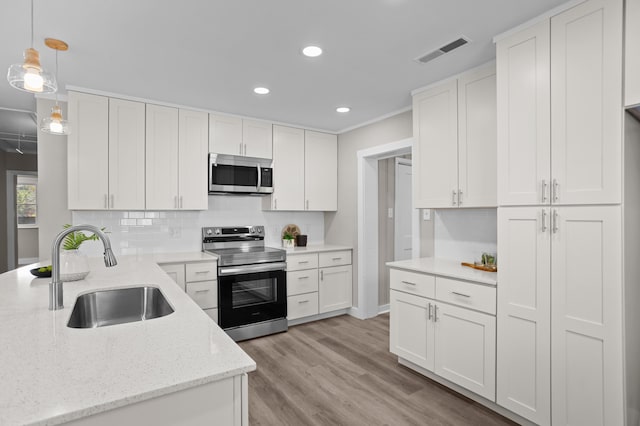 kitchen with sink, appliances with stainless steel finishes, hanging light fixtures, light stone counters, and white cabinets