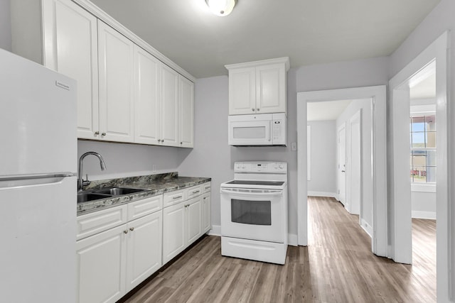 kitchen with white appliances, light hardwood / wood-style floors, white cabinetry, dark stone counters, and sink