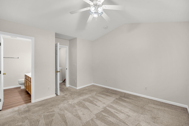 unfurnished bedroom featuring ceiling fan, ensuite bath, light colored carpet, and lofted ceiling