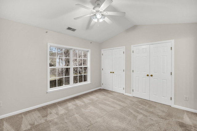 unfurnished bedroom featuring ceiling fan, light colored carpet, vaulted ceiling, and multiple closets