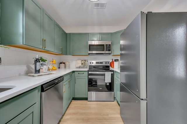 kitchen featuring decorative backsplash, light wood-type flooring, stainless steel appliances, and green cabinetry