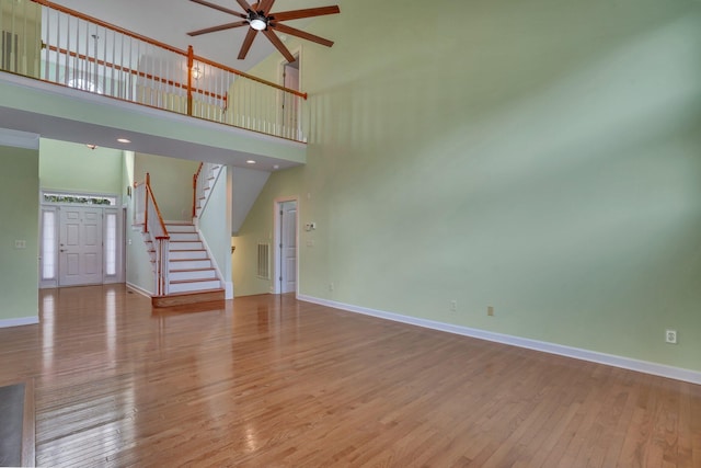 unfurnished living room featuring light wood-type flooring, a towering ceiling, baseboards, and stairs