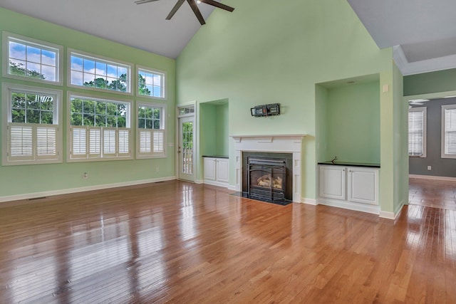 unfurnished living room with ceiling fan, baseboards, a healthy amount of sunlight, a fireplace with flush hearth, and wood finished floors