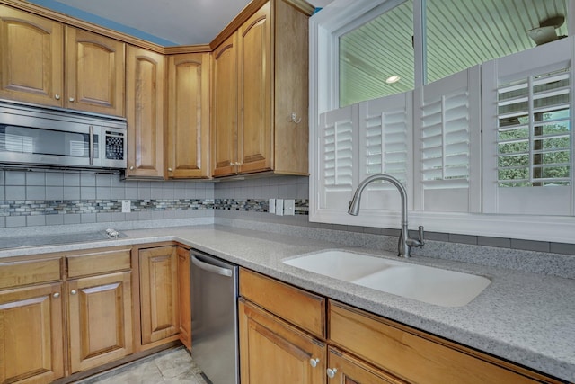 kitchen with a sink, brown cabinets, decorative backsplash, stainless steel appliances, and light stone countertops