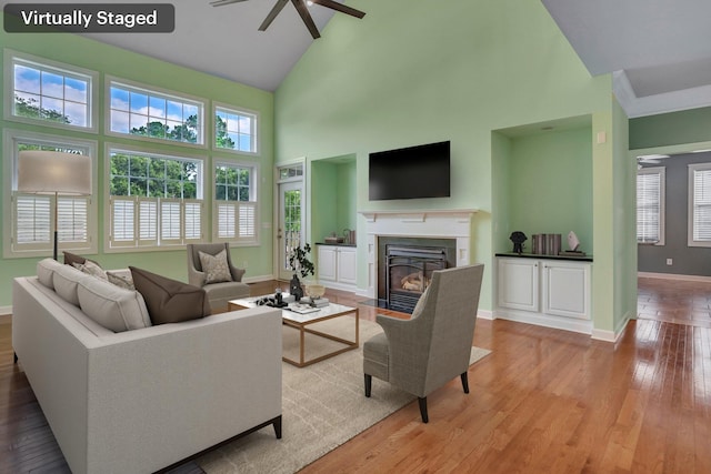 living area with ceiling fan, baseboards, high vaulted ceiling, a fireplace with flush hearth, and light wood-type flooring