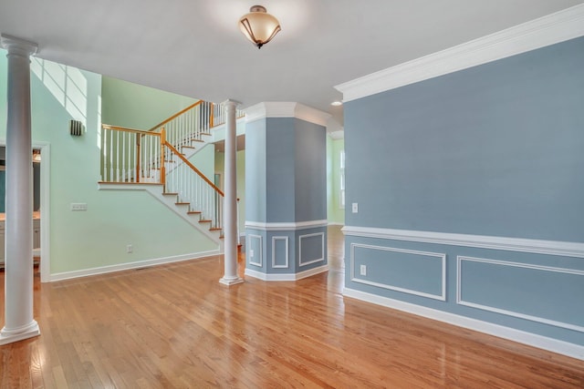 empty room featuring crown molding, stairs, wood finished floors, decorative columns, and a decorative wall