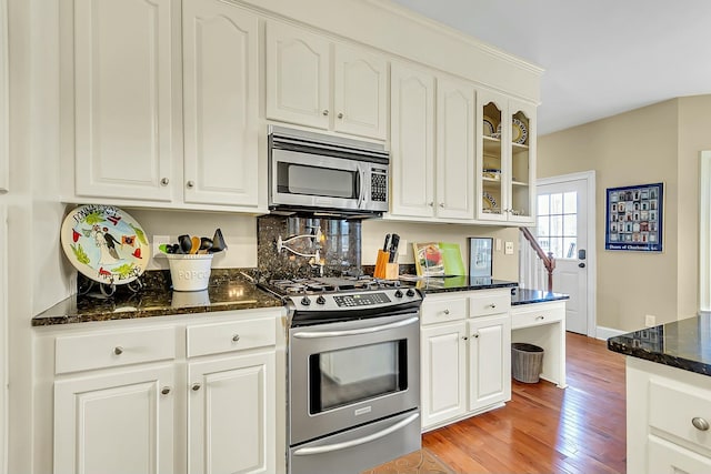 kitchen featuring dark stone counters, glass insert cabinets, stainless steel appliances, light wood-style floors, and white cabinetry