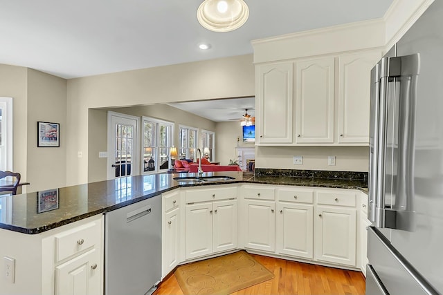 kitchen featuring stainless steel appliances, white cabinets, a sink, dark stone countertops, and a peninsula